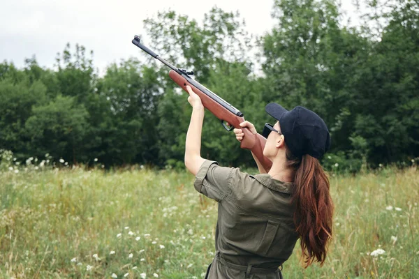 Military woman holding gun up sight hunting back view black cap — Stock Photo, Image