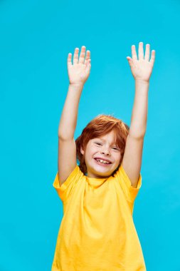 Mavi arka planda elleri havada kızıl saçlı çocuk kahkahalar atıyor. 