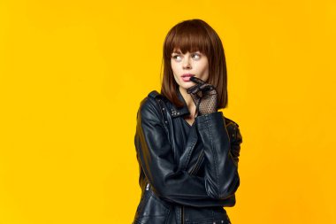 Siyah elbiseli ve eldivenli, parlak sarı arka planda bir kadın.