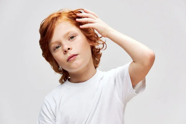 Pelirroja niño sosteniendo la mano cerca de la cabeza recortada vista camiseta blanca — Foto de Stock