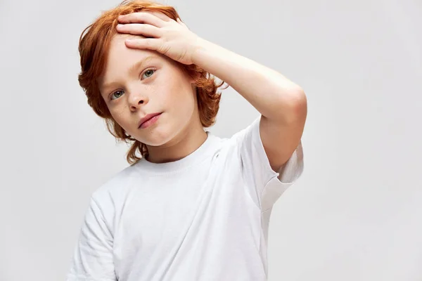 Roodharige tiener houdt een hand op zijn hoofd wit t-shirt kindertijd — Stockfoto
