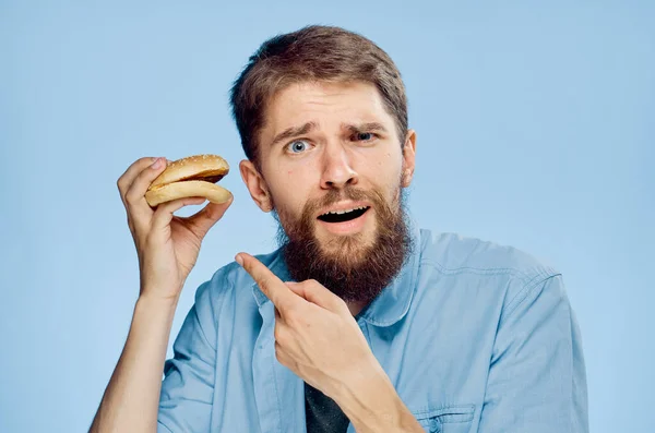 Um homem com um hambúrguer nas mãos um lanche fast food camisa azul com gravata — Fotografia de Stock
