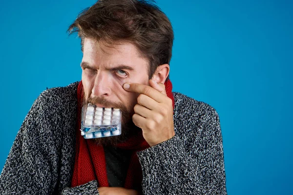 Чоловік з таблетками на синьому фоні здоров'я медицина і теплий одяг . — стокове фото