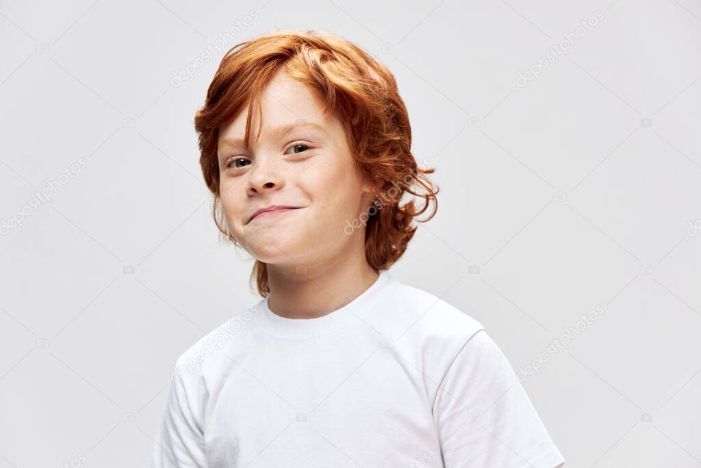 Cheerful red-haired child in a white T-shirt smile studio close-up 