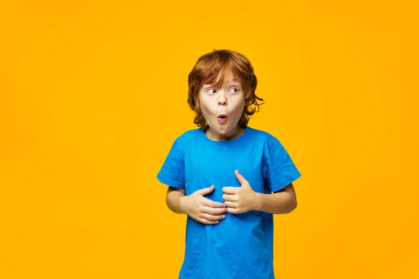 Κοκκινομάλλα παιδί έκπληξη μπλε t-shirt κίτρινο φόντο παιδική ηλικία — Φωτογραφία Αρχείου