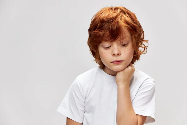 Sorgsen rödhårig pojke ser ner hålla sin hand på hakan — Stockfoto