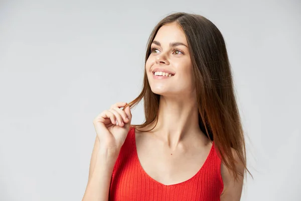 Lycklig kvinna i röd T-shirt vidrör håret med händerna leenden och ser åt sidan närbild — Stockfoto
