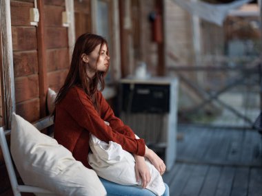 Kadın terasta bankta oturuyor, boş zamanlarında temiz hava alıyor.