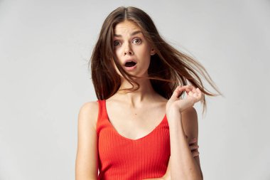 Kırmızı tişörtlü, ağzı açık bir kadın elleriyle saçına dokunuyor.