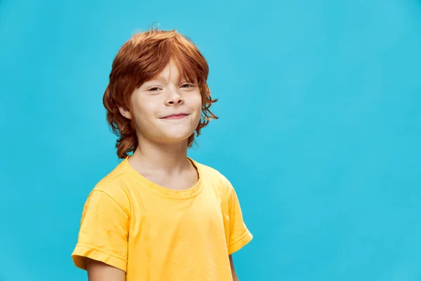 Niño sonriente de pelo rojo con una camiseta amarilla sobre un fondo azul —  Fotos de Stock