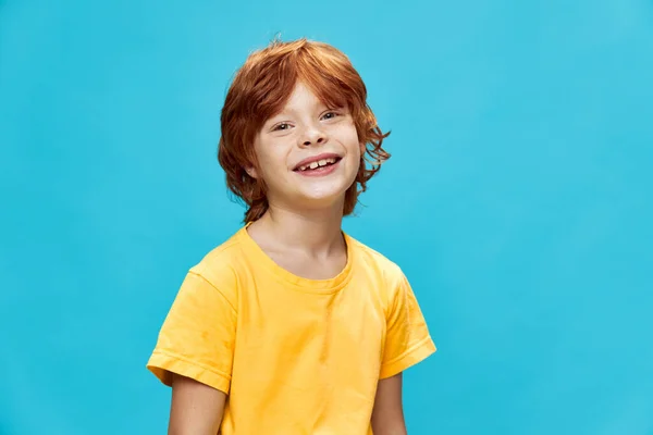 Pojkläge med ett vackert leende och en gul t-shirt blå bakgrund — Stockfoto