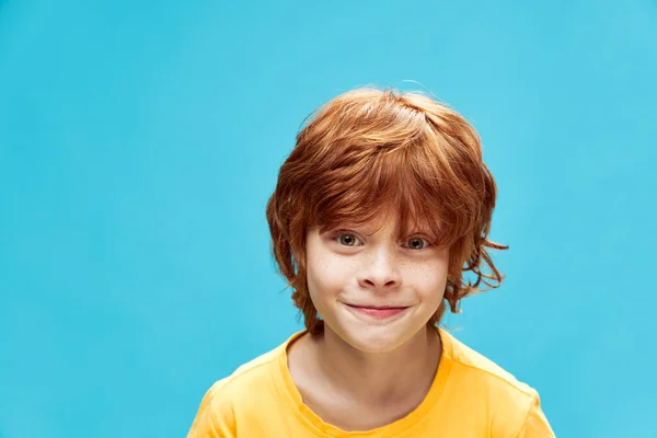 Piros hajú gyermek sárga pólóban, kék háttérrel — Stock Fotó