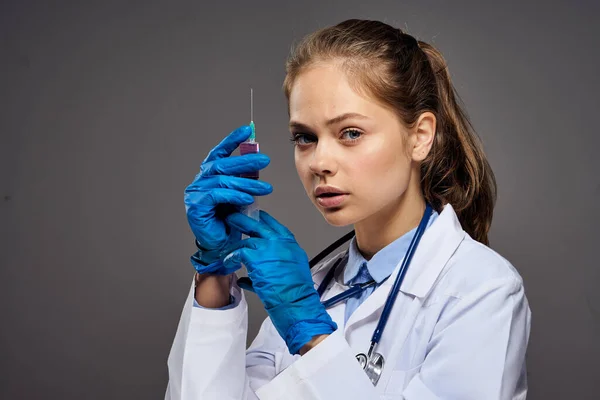 Žena lékař v lékařských šatech se stetoskopem kolem krku injekční stříkačka brýle internista šedé pozadí — Stock fotografie