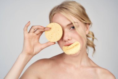 Çıplak omuzlu bir sarışın yüzüne pamuk pedleri tutar.