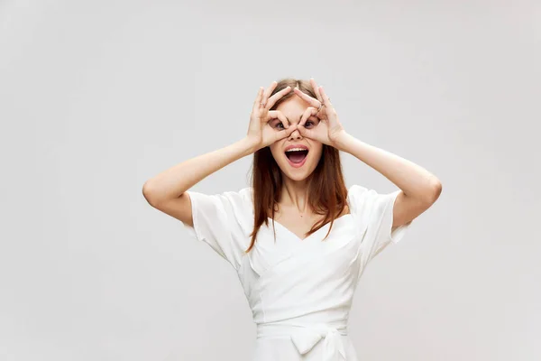 Mujer sostiene sus manos cerca de su cara en forma de una máscara sonrisa vestido blanco — Foto de Stock