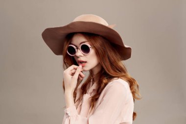  Bej makyajlı, şapkalı ve gömlekli kızıl saçlı kadın gülümsemesi gençleri cezbediyor.