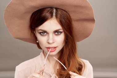  Bej makyajlı, şapkalı ve gömlekli kızıl saçlı kadın gülümsemesi gençleri cezbediyor.