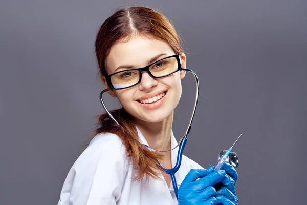 Ärztin im Arztkittel und blauen Handschuhen mit Stethoskop und Dokumenten auf grauem Hintergrund — Stockfoto