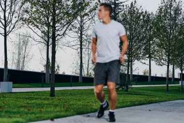 Şortlu bir adam spor için doğada bir parka gider ve bir model spor ayakkabı giyer.