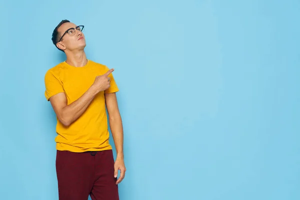 Homme émotionnel il gestes avec sa main jaune t-shirt lunettes bleu isolé fond Copier l'espace — Photo