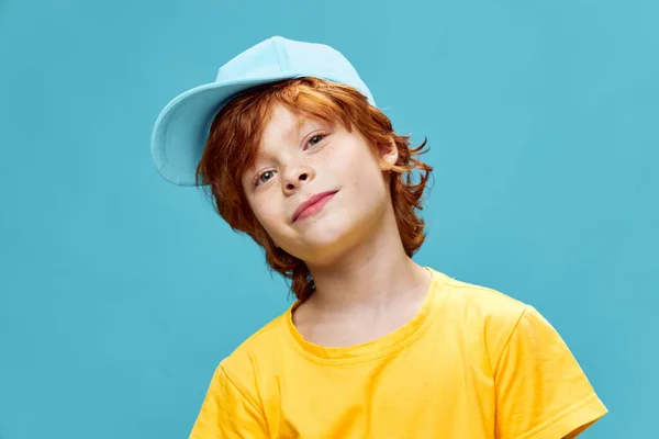 노란 티셔츠를 입고 파란 모자를 쓴 아이가 옆으로 머리를 기울여서 — 스톡 사진