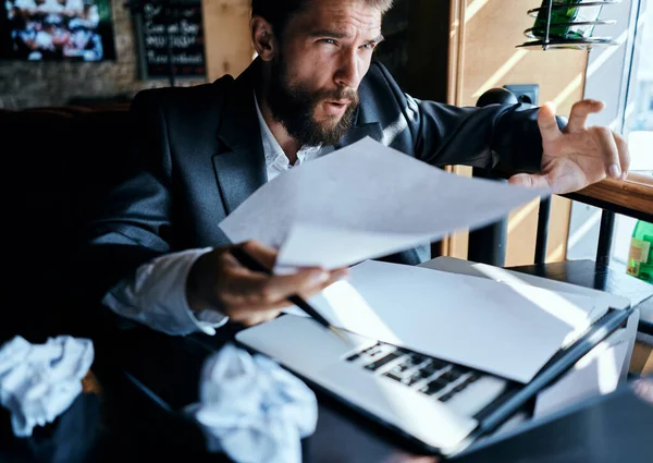 Uomo d'affari in un caffè seduto al tavolo documenta laptop carta spiegazzata stile di vita esecutivo emozioni — Foto Stock