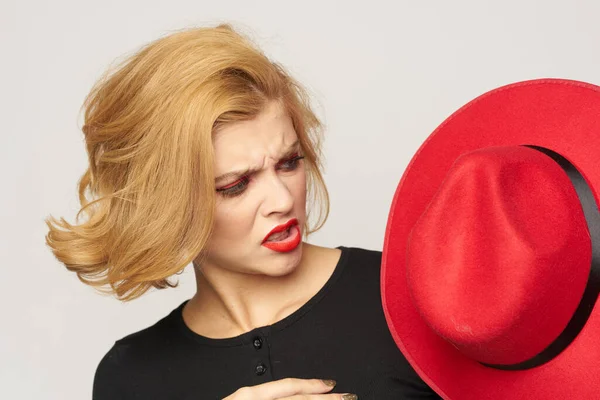 Nette blonde kurzhaarige rote Mütze in der Hand Nahaufnahme Licht Hintergrund — Stockfoto