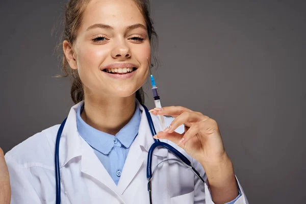 Médico mulher em vestido médico com estetoscópio em torno de sua seringa pescoço injeção óculos estagiário fundo cinza — Fotografia de Stock