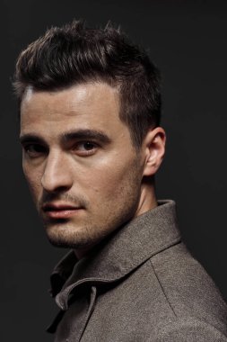 Genç ve yakışıklı bir adam karanlık arka planda kameraya bakıyor. Stüdyo çekimi  