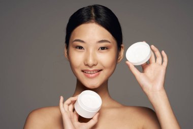 Genç, güzel, gülümseyen Asyalı kadın krem tutuyor. 