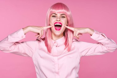 Pembe peruklu genç kadın pembe arka planda yanaklarını stüdyoda gösteriyor.