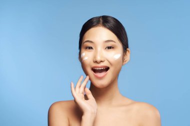 Güzel Asyalı bir kadının portresi izole edilmiş arka planda krem sürüyor.