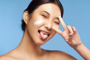 Genç Asyalı kadın stüdyoda mavi arka planda el kol hareketi yapıyor. 