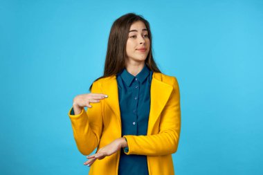  Sarı ceketli güzel bir kadın stüdyoda mavi arka planlı bir şey gösteriyor..