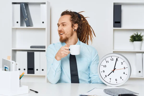若いビジネスマンがカップと時計を持ってオフィスに座っている — ストック写真
