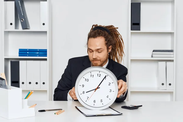 若いビジネスマンが時計を持ってオフィスに座っている — ストック写真