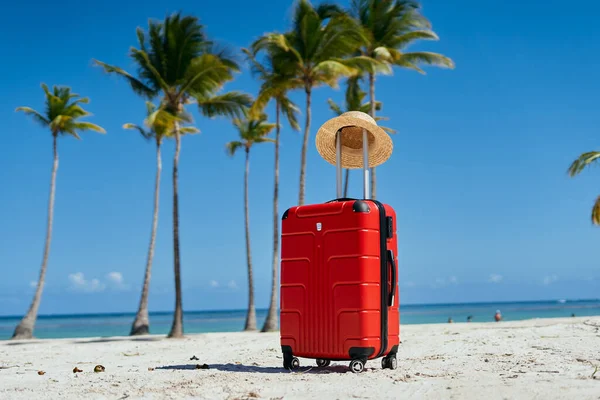 red suitcase and straw hat on th e beach