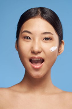 Stüdyoda mavi arka planda ağzı açık Asyalı genç bir kadın. 