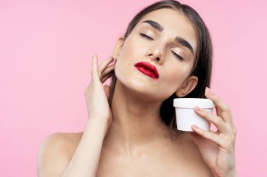 Güzel bir kadının portresi pembe arka planda güzellik ürünü taşıyor.