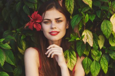 Saçında çiçekle poz veren genç ve güzel bir kadın kameraya bakıyor. 