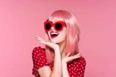 Pembe peruklu ve pembe arka planda güneş gözlüklü mutlu kadın.
