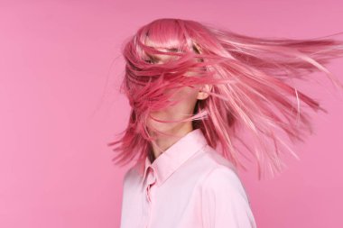 Pembe peruklu güzel bir kadının pembe arka planda saçlarını çekerken sudio çekimi.