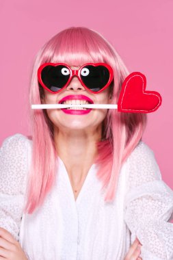 Pembe peruklu ve pembe arka planda kalbi olan güneş gözlüklü kadın. 