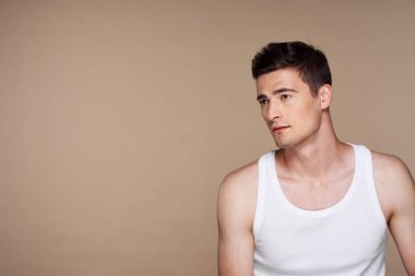 Stüdyo çekimi. Bej rengi üzerinde poz veren genç yakışıklı adamın portresi.