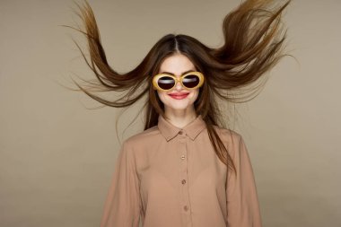  Güneş gözlüklü genç bir kadın bej arka planda yalnız poz veriyor.  