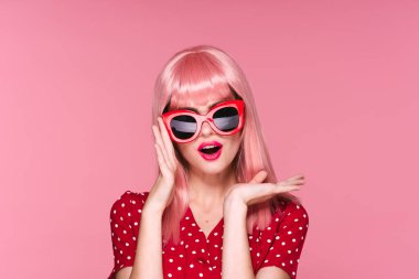 Pembe peruklu ve güneş gözlüklü kadın pembe arka planda poz veriyor.
