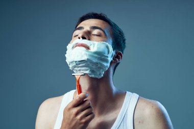 Stüdyo çekimi. Genç yakışıklı adam koyu mavi arka planda tıraş oluyor.