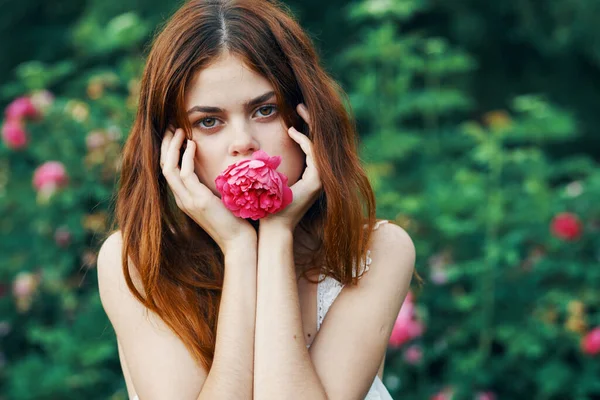 庭に赤い花を持つ若い美しい女性 — ストック写真