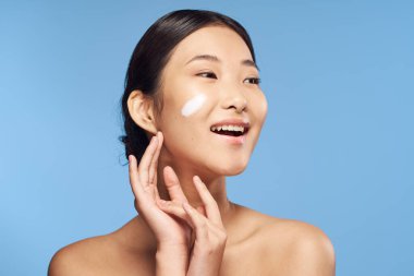 Genç Asyalı bir kadın mavi arka plandan stüdyoya bakıyor. 