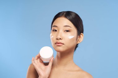 Stüdyoda mavi arka planda krem gösteren genç Asyalı kadın. 